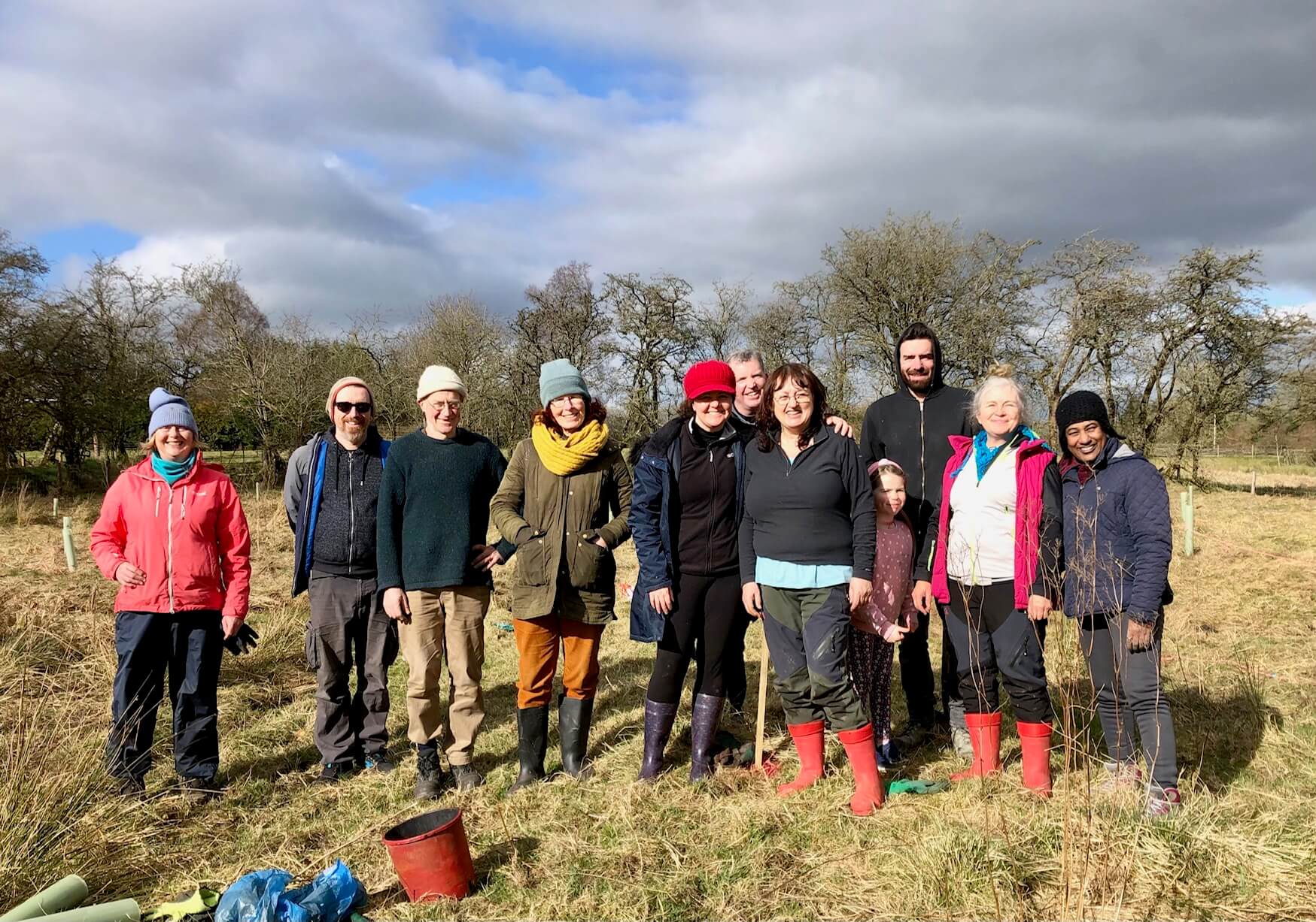 Happy group of volunteers in a sunny field. Some wearing wellies and some wearing winter hats